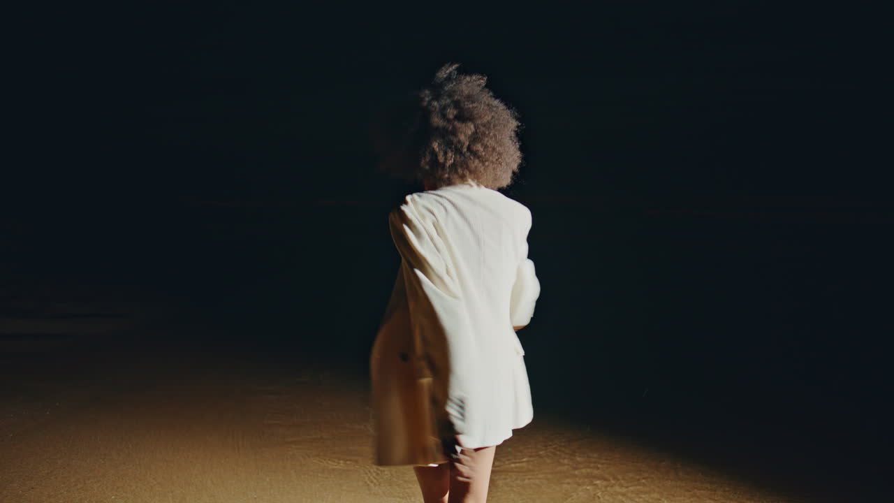 Modella di moda che balla sulla spiaggia di notte. Donna attraente che si diverte camminando tra le onde.