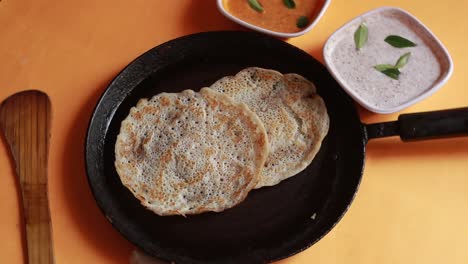 rotating oothappam - dosa - south indian breakfast using rice lentil and vegetables served with coconut chutneyisolated on yellow background