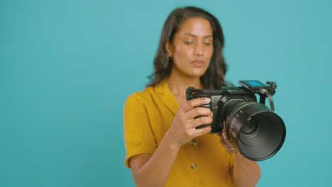 mature female videographer with camera filming video against blue background on shoot in studio