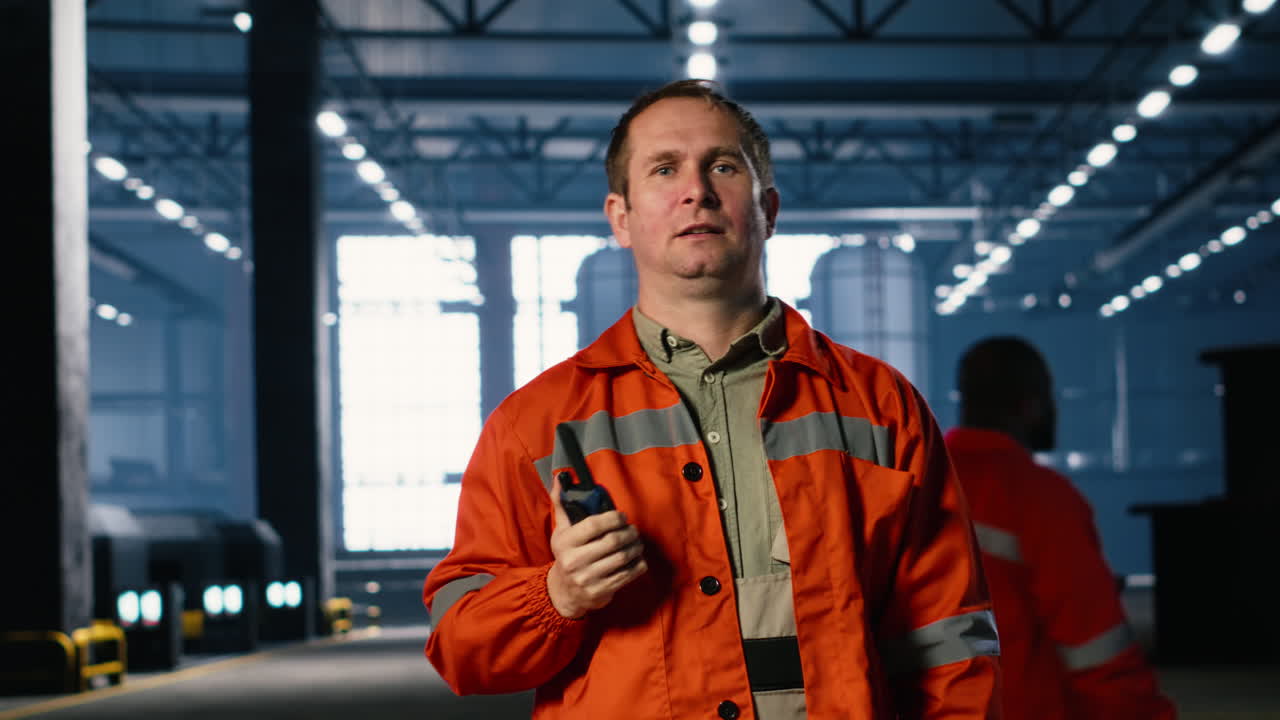 Heavy industry employee speaks into walkie talkie device in warehouse