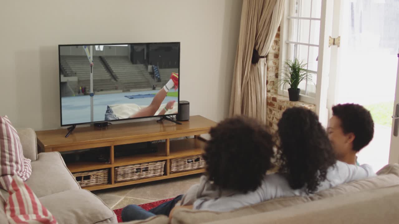 Famiglia felice seduta a casa insieme che guarda l'atletica salto in alto in TV