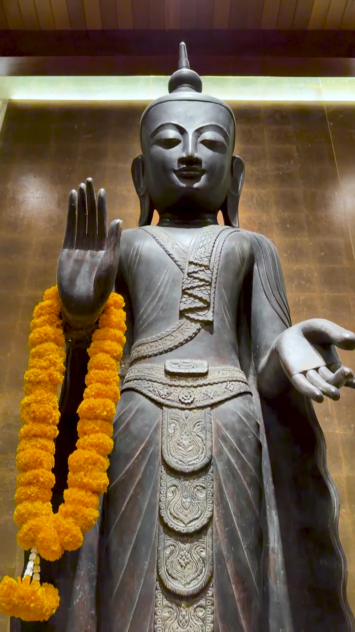 Un'inclinazione verticale della telecamera rivela una statua di Buddha in bronzo in piedi adornata con ghirlande di calendule gialle.