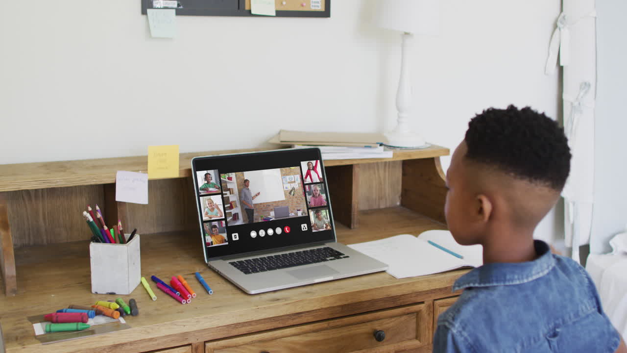 Schoolboy using laptop for online lesson at home, with diverse teacher and class on screen