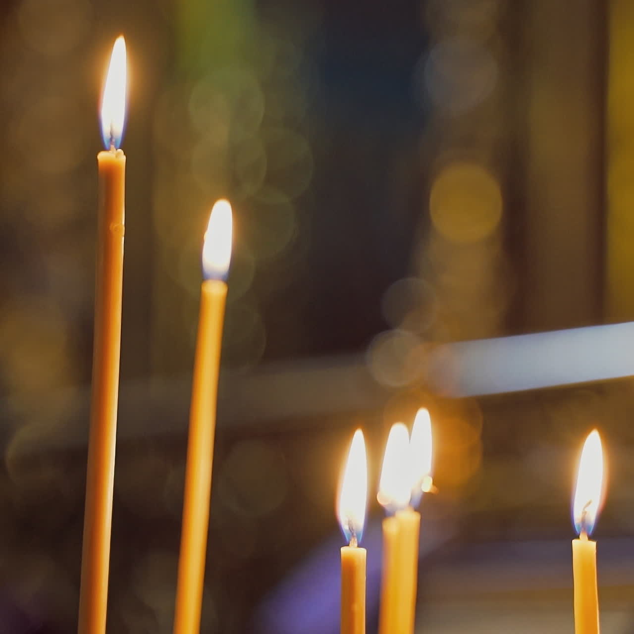 Beeswax candles are glowing on the blurred background. Church candles burning in the night temple. Candles are lit for prayer intentions.