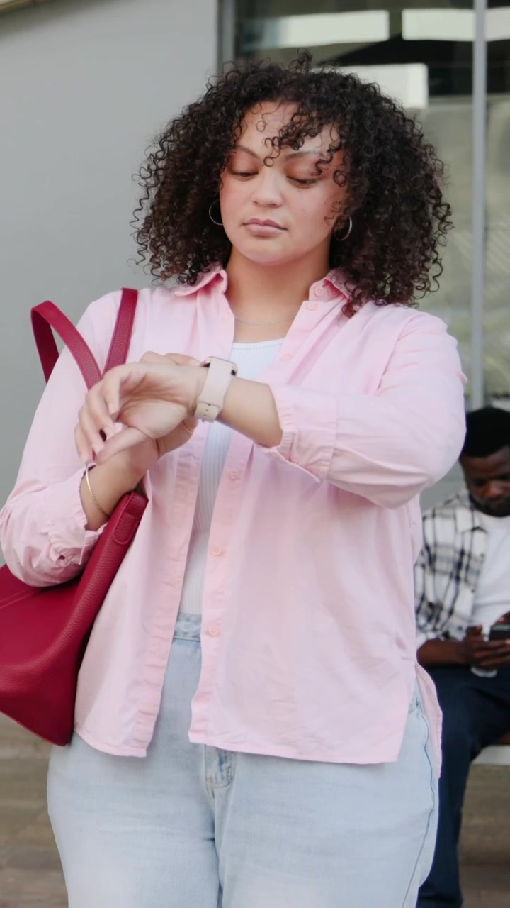 Vertical video: Arriving at entry, woman in pink shirt checking watch for time, adjusting red tote