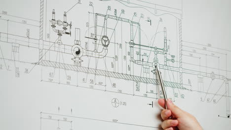 a hand pointing at a detailed engineering blueprint