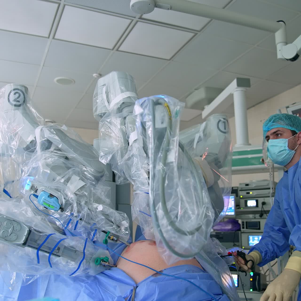 Confident surgeon holding the surgical instrument and watching the work of robotic equipment at the screen. Well-equipped operational theatre at background