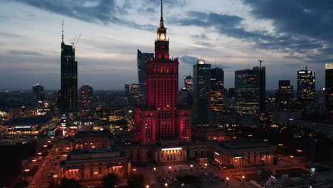 Red-illuminated-monumental-high-rise-Palace-of-Culture-and-Science-and-downtown-skyscrapers-at-twilight-time.-Warsaw,-Poland