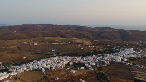 aerial flyover of kythnos chora during a glowing summer sunset, capturing traditional white houses bathed in golden light and surrounded by peaceful hills