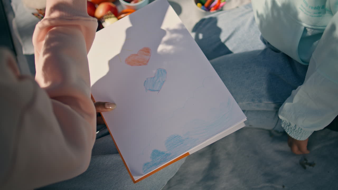 娘と一緒に夏のピクニックに座っている母親の手がアルバムを描いています