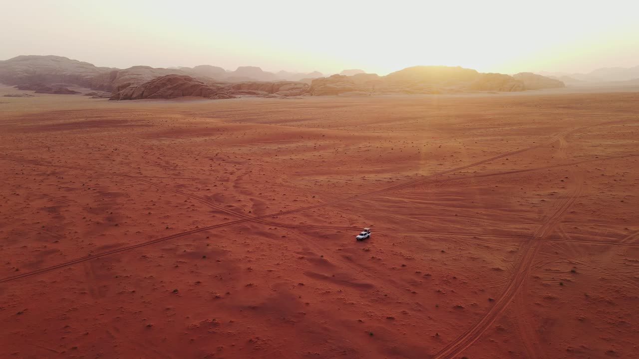 White jeep drives through Wadi Rum desert, the drone captures the sunset scenery