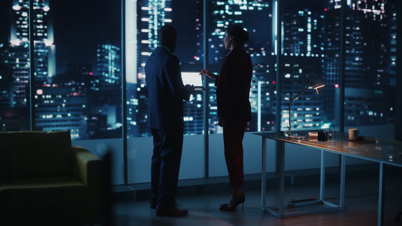 el ceo de una empresa exitosa está hablando, usando una computadora portátil mientras está de pie en una oficina de la gran ciudad por la noche. dos gerentes exitosos discuten el crecimiento estadístico, la fusión para el proyecto de comercio electrónico