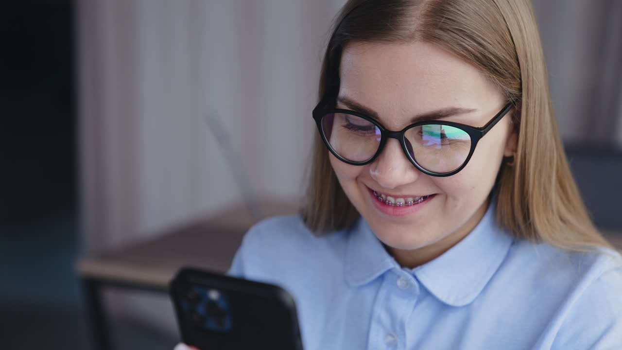 Fair-haired woman in glasses holding phone and looking into it. Portrait of a lady working on her phone. Close up. High angle view.
