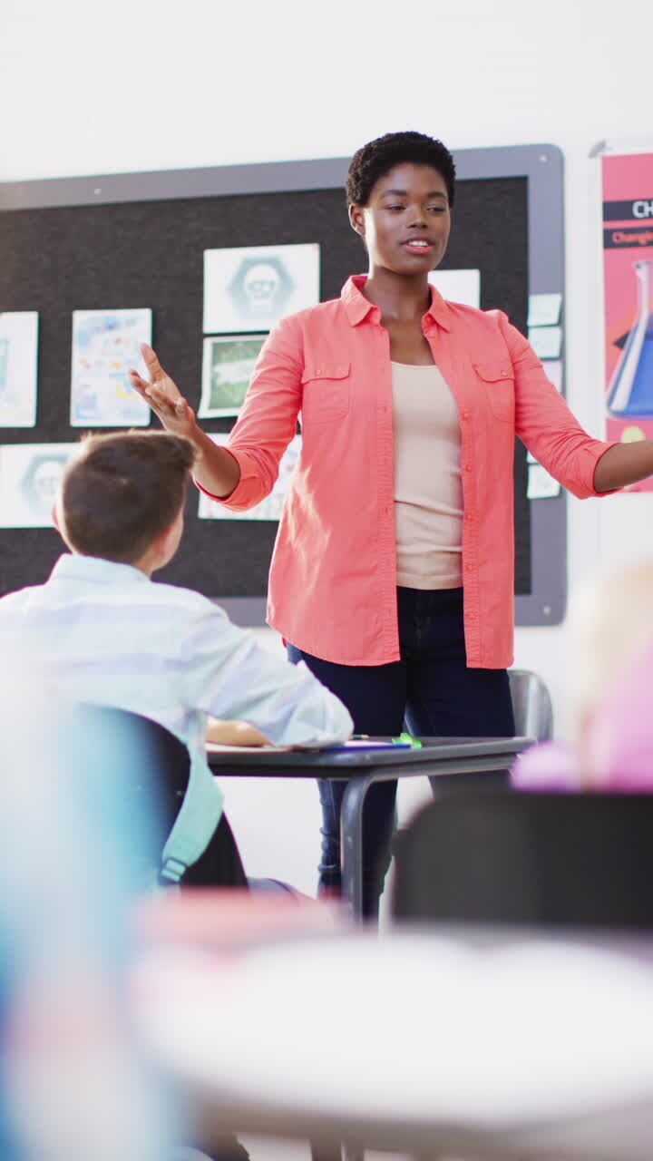 Vertical video of happy diverse female teacher and schoolchildren in school classroom
