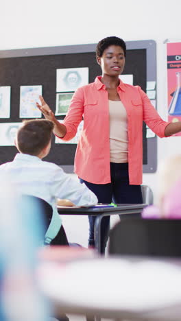 vertical video of happy diverse female teacher and schoolchildren in school classroom