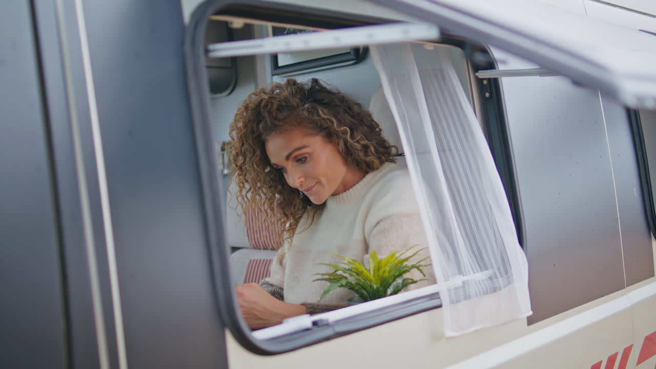 Bella viaggiatrice seduta alla finestra del camper che guarda lo smartphone, primo piano.