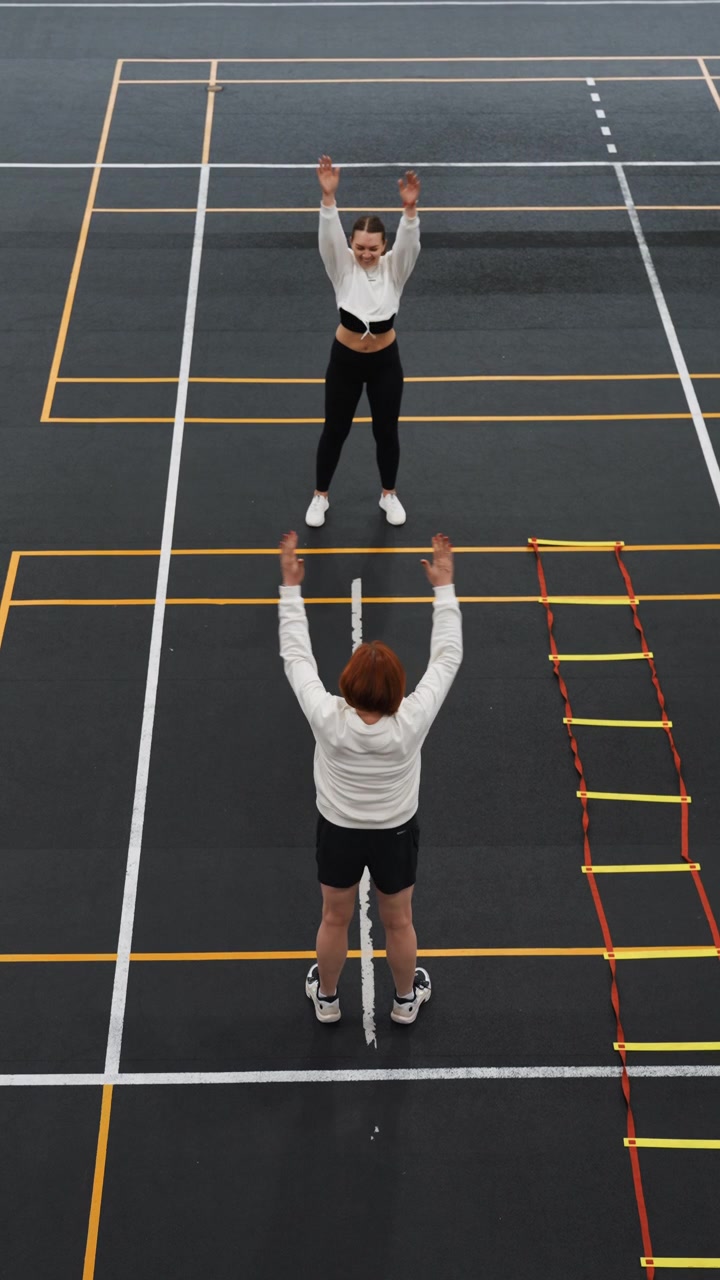 Partners celebrate badminton rally on court, aerial view of two players exchanging raisedarm celebration and friendly gestures beside agility ladder, lively energy, smiles, shared teamwork and warm