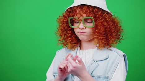 joven pelirroja pensativa con gafas y sombrero de panama contando en los dedos hasta cinco, fondo de llave de croma verde