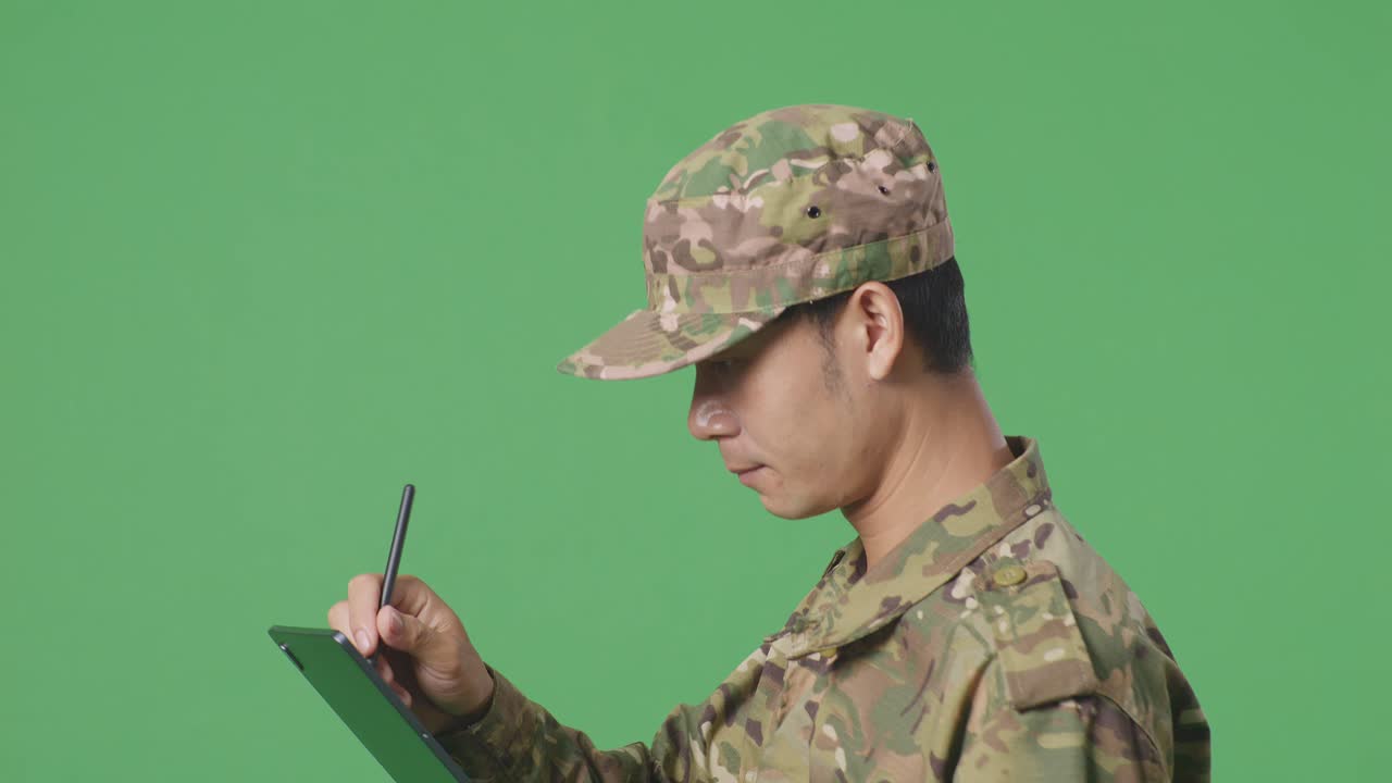 녹색 스크린 배경 스튜디오에서 는 동안 태블릿에 메모를 취하는 아시아 남자 군인