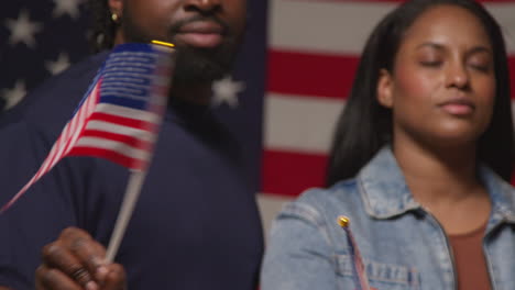 retrato de estudio de una pareja agitando banderas en miniatura de estrellas y rayas frente a la bandera estadounidense celebrando la fiesta del día de la independencia del 4 de julio