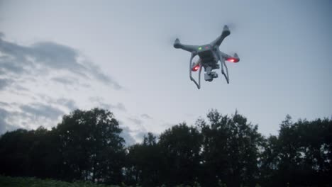 Eine-Fliegende-Drohne-Blinkt-Vor-Einigen-Bäumen-Und-Dem-Bewölkten-Himmel