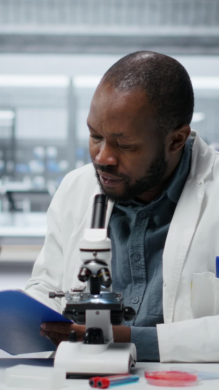 Ricercatore del Vertical video Lab che guarda attraverso le lenti di un microscopio scientifico per studiare le cellule