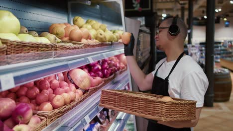 man worker in black apron and gloves stocking the fruits in supermarket while listen to the music