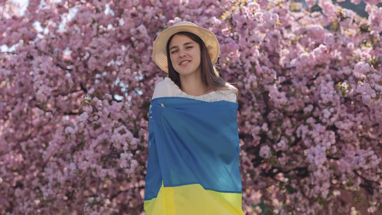 Young Woman with Ukrainian Flag in a Blooming Cherry Blossom Garden