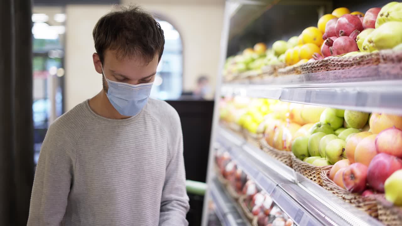 마스크를 입은 남자가 식품 선반에서 신선한 사과를 꺼낸다. 쇼핑객이 식료품 가게에서 사과를 선택한다.