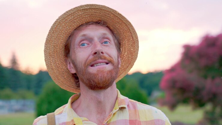 Nærbillede af en smilende mand med stråhat, der ser op ved solnedgang