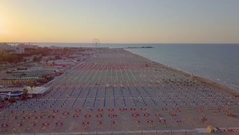 aerial view of rimini beach at adriatic coast in italy with colorful parasols and sunbeds on the sand and ferris wheel in a distance on a beautiful morning.