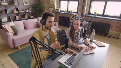 vista superior de un hombre y una mujer jóvenes con auriculares sentados en una mesa con micrófonos mientras graban un podcast 1