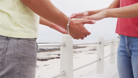 Mid-section-of-african-american-young-couple-holding-hands-on-the-promenade-near-the-beach