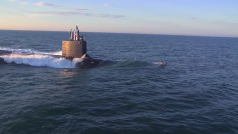 aerials over a submarine at sea with dolphins jumping across bow