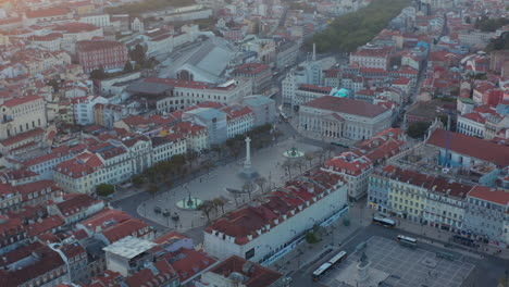 Aerial-rotating-view-of-column-of-Pedro-IV-in-small-public-square-in-downtown-city-center-Lisbon,-Portugal-surrounded-by-colorful-traditional-European-houses