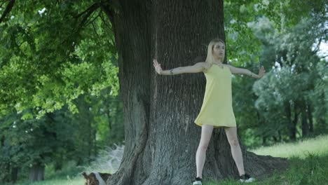 woman in yellow dress dancing by tree in summer park