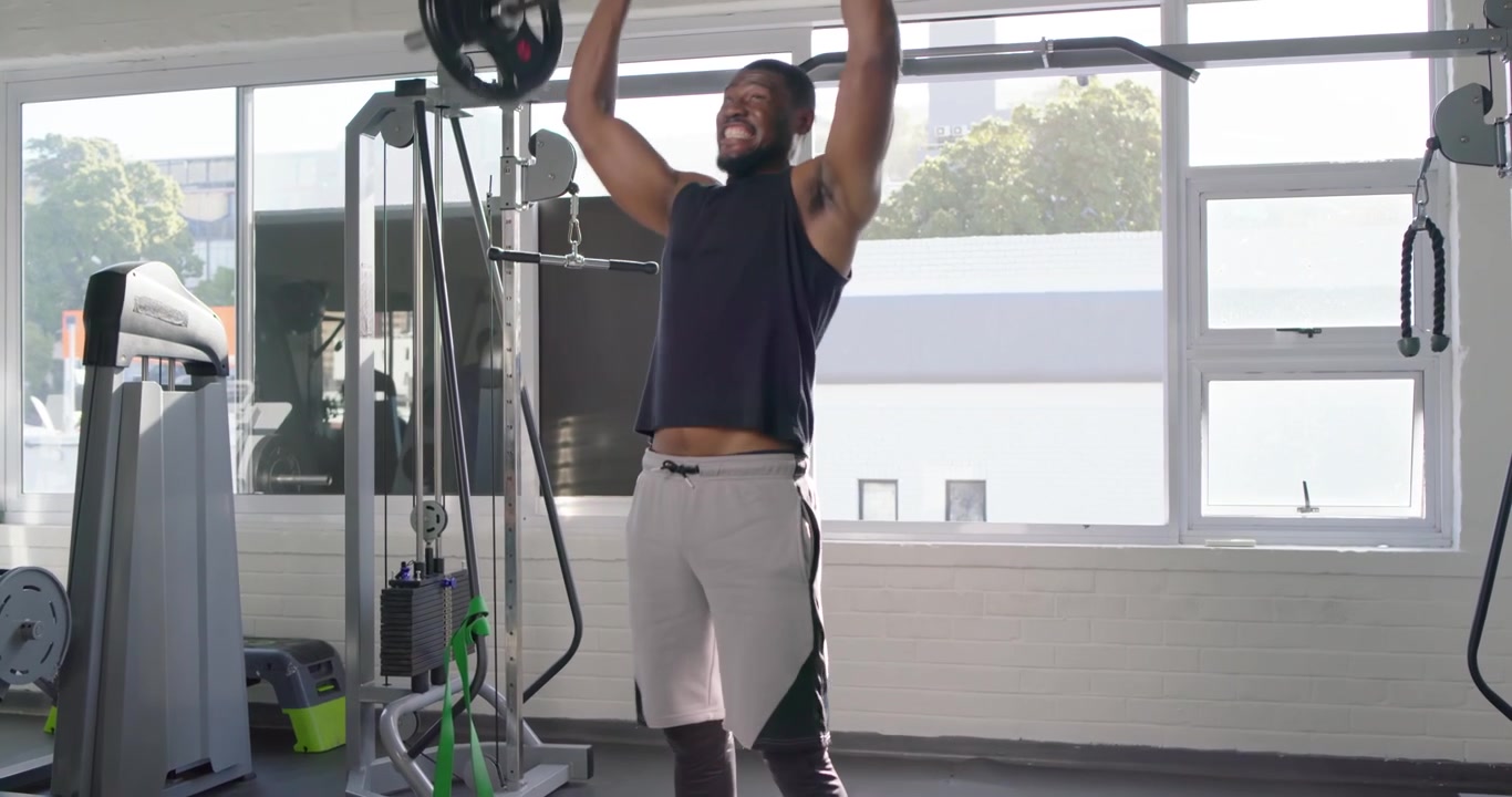 Man in sleeveless top starting with barbell at shoulders, pressing, deadlifting for strength in gym