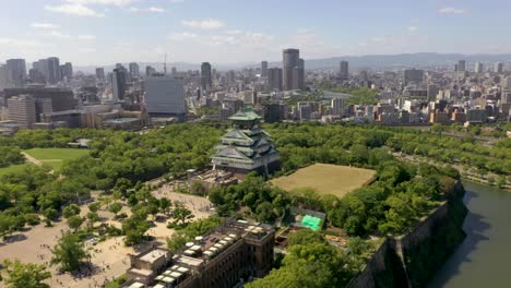 Aerial-of-famous-landmark-Osaka-Castle-with-park,-moat,-skyscrapers,-and-city-in-Osaka,-Japan