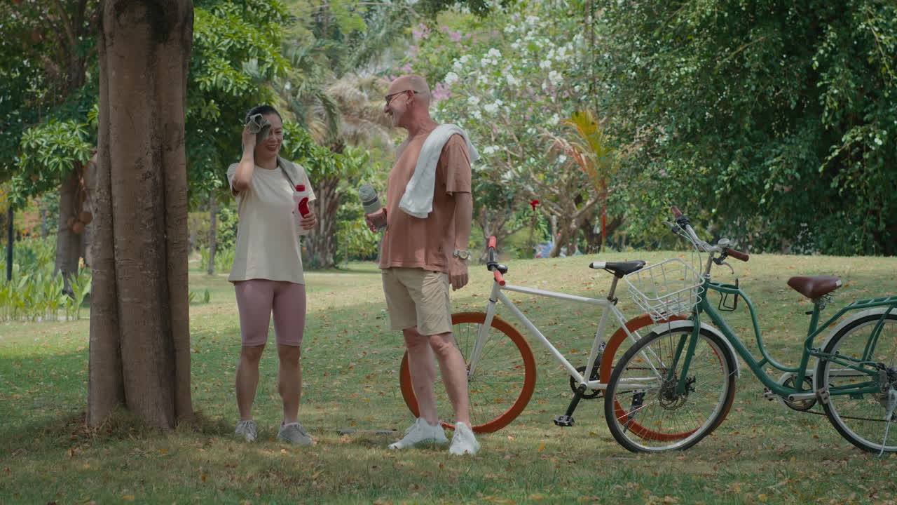 Spouses Coming to Rest near Tree after Bicycle Ride in Park