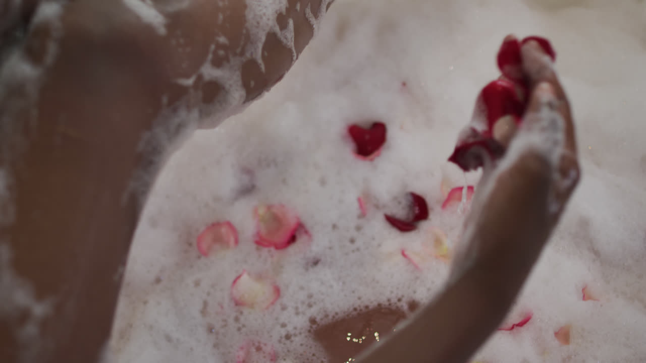 Hands of african american attractive woman taking bath with foam and rose petals