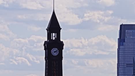 detailed view of the historic lackawanna clock tower against a cloudy sky, with a modern glass skyscraper partially visible