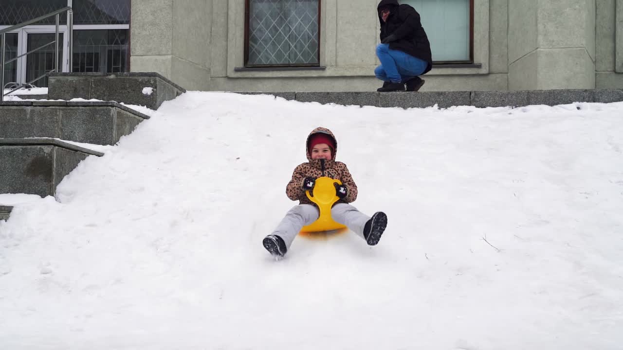 padre empujando a un niño en un platillo de nieve bajando una colina