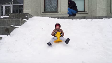 father pushing kid on snow saucer riding down hill