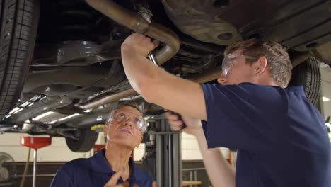 mecánico y aprendiz masculino trabajando juntos debajo de un coche