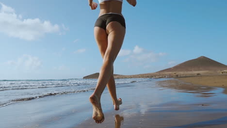 fitness runner woman running on beach listening to music motivation with phone case sport armband strap. sporty athlete training cardio barefoot with determination under summer sun.