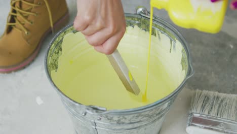 hand mixing yellow wall paint in bucket