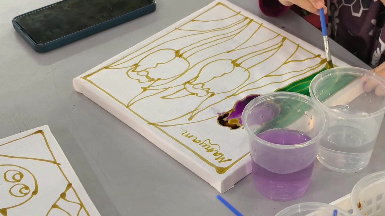 Close-up of a child painting colorful dye on a traditional Malaysian batik canvas. Young student learning cultural heritage craft through hands-on art. Educational activity introducing authentic folk