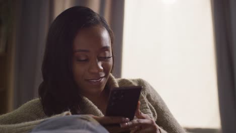 close up of young woman relaxing at home sitting on sofa scrolling through mobile phone