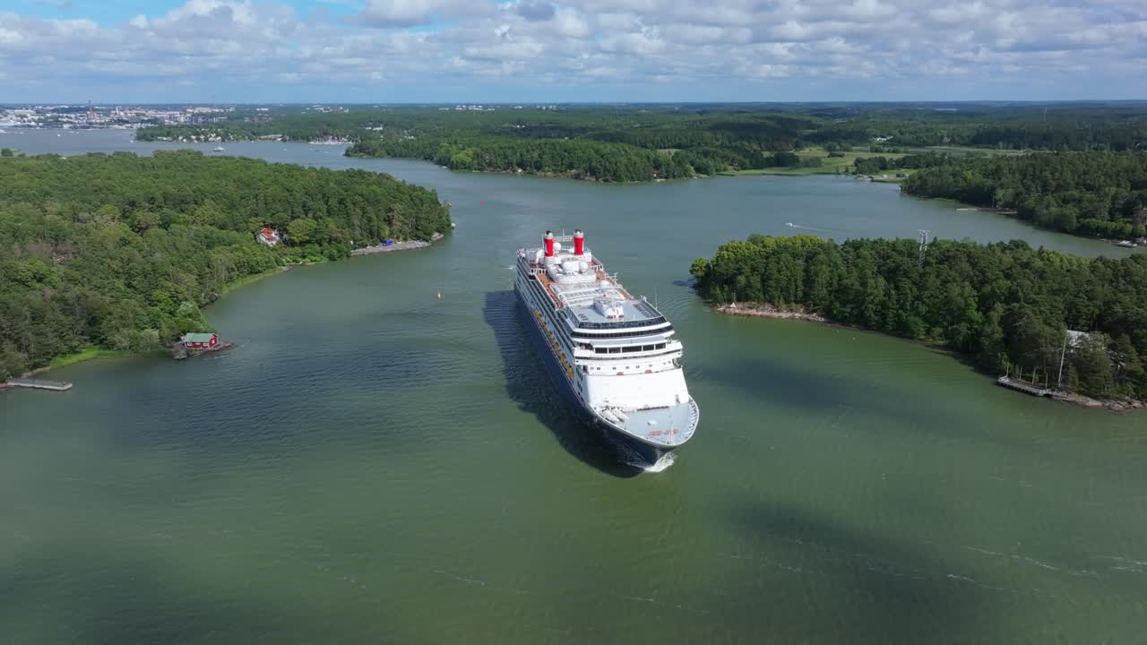 Fred.Olsen Cruise Lines passenger ship BOREALIS making way ahead in Finnish archipelago on departure. Vessel passing between islands. Tug boat following. High altitude aerial view crossing bow.