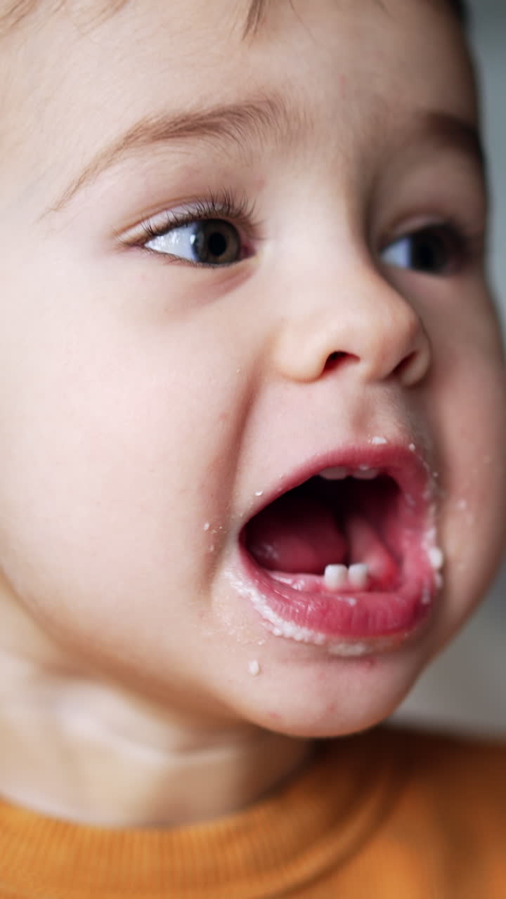 Adorable little kid opens wide his mouth showing few teeth. Baby boy takes a bagel to bite and then is given a spoon of food. Close up. Vertical video